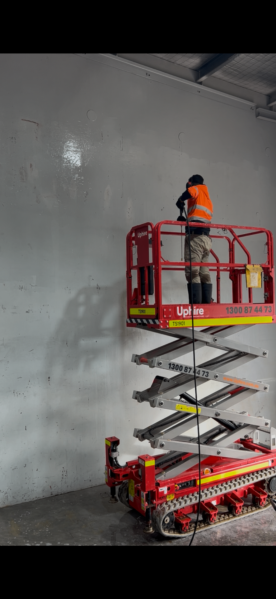Worker on a scissor lift cleaning an interior warehouse wall